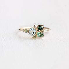 three stone ring with green and blue stones on top, sitting on a white surface