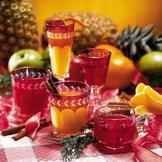 several glasses filled with different colored liquids on a table next to apples and oranges