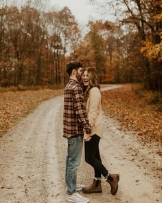 a couple holding hands and walking down a dirt road in the fall with leaves on the ground