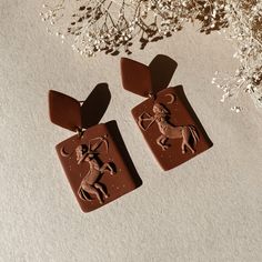 two chocolate pendants with an image of a man riding a horse on them, sitting next to some flowers