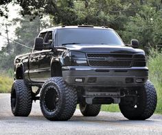 a large black truck parked on the side of a road next to some grass and trees