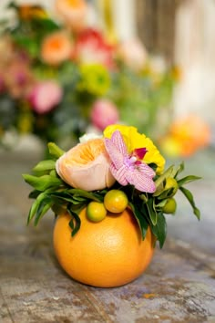 an orange vase filled with flowers and fruit