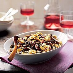 a white bowl filled with pasta next to two glasses of red wine on a table