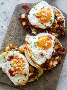 three breakfast tacos with eggs and meat on a wooden cutting board next to some condiments