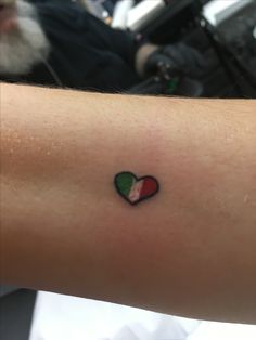 a small heart tattoo on the arm with an italian flag in the shape of a heart