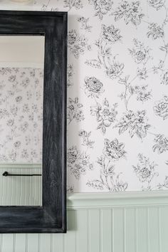 a black framed mirror sitting on top of a wooden shelf next to a wallpapered wall