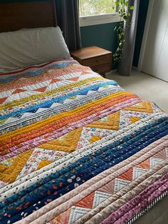 a bed with a colorful quilt on it next to a dresser and window sill