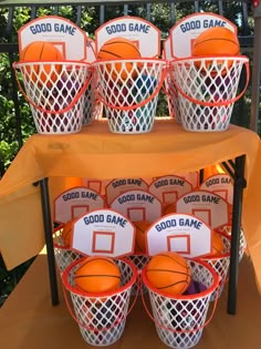 an orange table topped with baskets filled with basketballs next to hoop game signs and balls