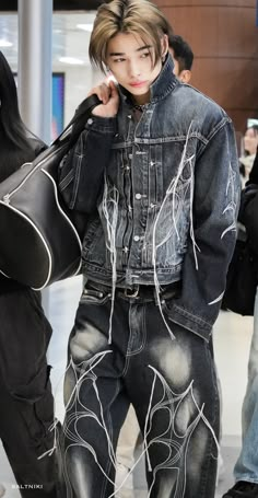 a man in black jacket and jeans holding a guitar case while standing next to other people