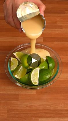 someone pouring dressing into a glass bowl filled with limes