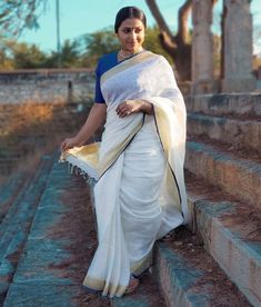 a woman wearing a white and blue sari walking up some steps with trees in the background