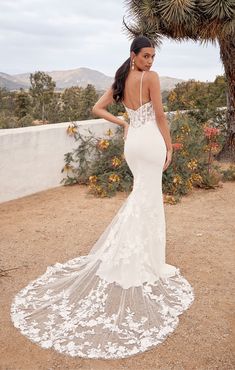 a woman in a white wedding dress standing next to a cactus tree with her back turned