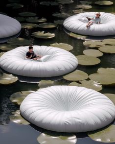 two people are sitting on bean bags floating in the water with lily pads around them