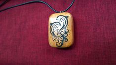 a wooden pendant with an image of a bird on it's side hanging from a cord