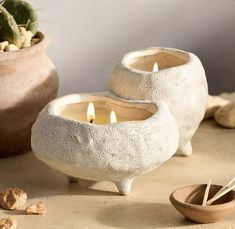 two white candles sitting on top of a table next to some rocks and a potted plant