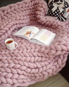 a coffee table with a pink blanket and book on it next to a cup of tea