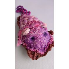 a stuffed animal with pink and purple colors on it's head, sitting on a white surface