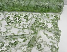 two pieces of green fabric on a white table cloth, one with leaves and flowers