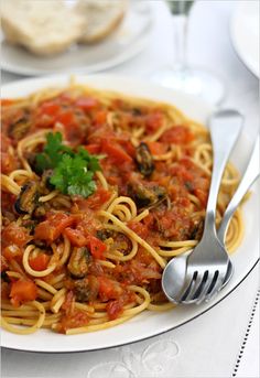 a plate of spaghetti with tomato sauce and parsley on the side next to bread