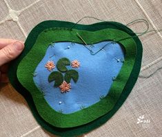 someone is stitching together some felt to make a heart shaped brooch pin cushion