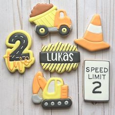 some decorated cookies are sitting on a white wooden surface with the number two and construction vehicles