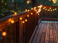 string lights are strung on the railing of a deck in front of trees and bushes