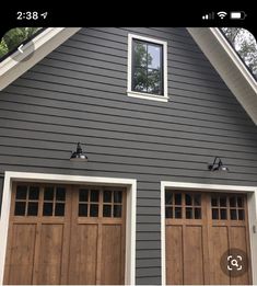 two brown garage doors in front of a gray house with white trim on the windows