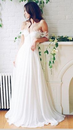 a woman standing in front of a brick wall wearing a white dress with flowers on it