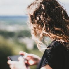 a woman looking at her cell phone while standing on top of a hill overlooking the city