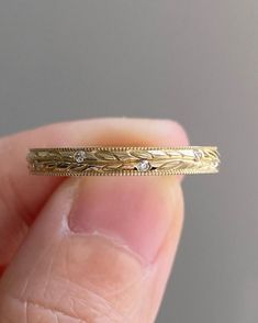 a close up of a person's finger holding a gold wedding band with diamonds