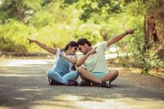 two people sitting on the ground with their arms around each other and pointing at something