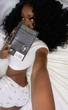 a woman laying in bed holding up a book to her face and looking at the camera