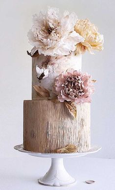 a three tiered cake decorated with flowers on a white plate and wooden board stand