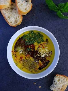 a white bowl filled with soup next to slices of bread on top of a blue surface