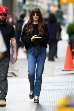 a woman in black sweater and jeans walking down the street with a man behind her