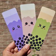 three different colored paper bookmarks in front of a brick wall with eyes and noses on them