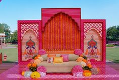 a stage set up for a wedding ceremony with flowers and decorations on the floor, in front of an orange backdrop