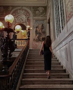 a woman is walking down the stairs in an old building with paintings on the walls