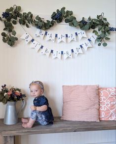 a baby sitting on a table next to a vase with flowers in it and a happy birthday banner