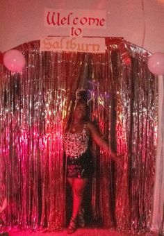 a woman standing in front of a welcome sign at a disco party with balloons and streamers