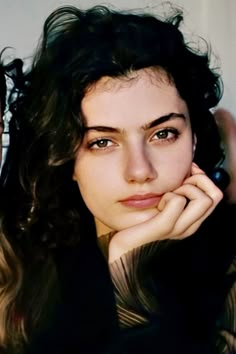 a close up of a person with long hair and wearing a black shirt, holding her hand to her face