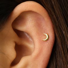 a woman's ear with a small gold crescent piercing