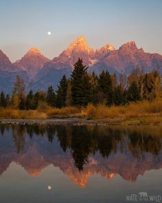 the mountains are reflected in the still water at sunset, while the moon is setting