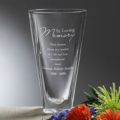 a memorial vase with flowers and greenery sits on a table in front of a gray background