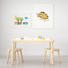 two children's tables and chairs in front of a wall with pictures on it