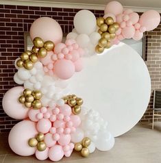 a large balloon arch with gold and pink balloons hanging from it's sides in front of a brick wall