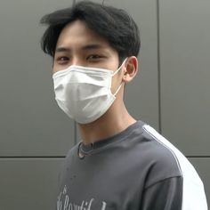 a young man wearing a face mask in front of a gray wall with black hair