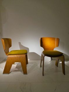 two wooden chairs sitting next to each other on a white floor in front of a wall