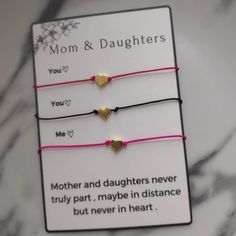 three bracelets with gold hearts on pink string and mother's day message attached to them