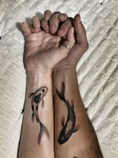 two people are holding hands with tattoos on their arms, both have black and white fish in them